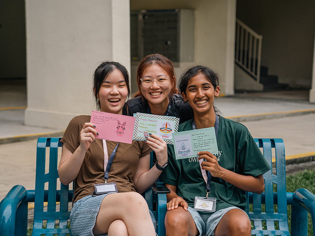 Ru Xin, Alicia and Harini (left to right) holding onto the cards they distributed for Deepavali 2023.